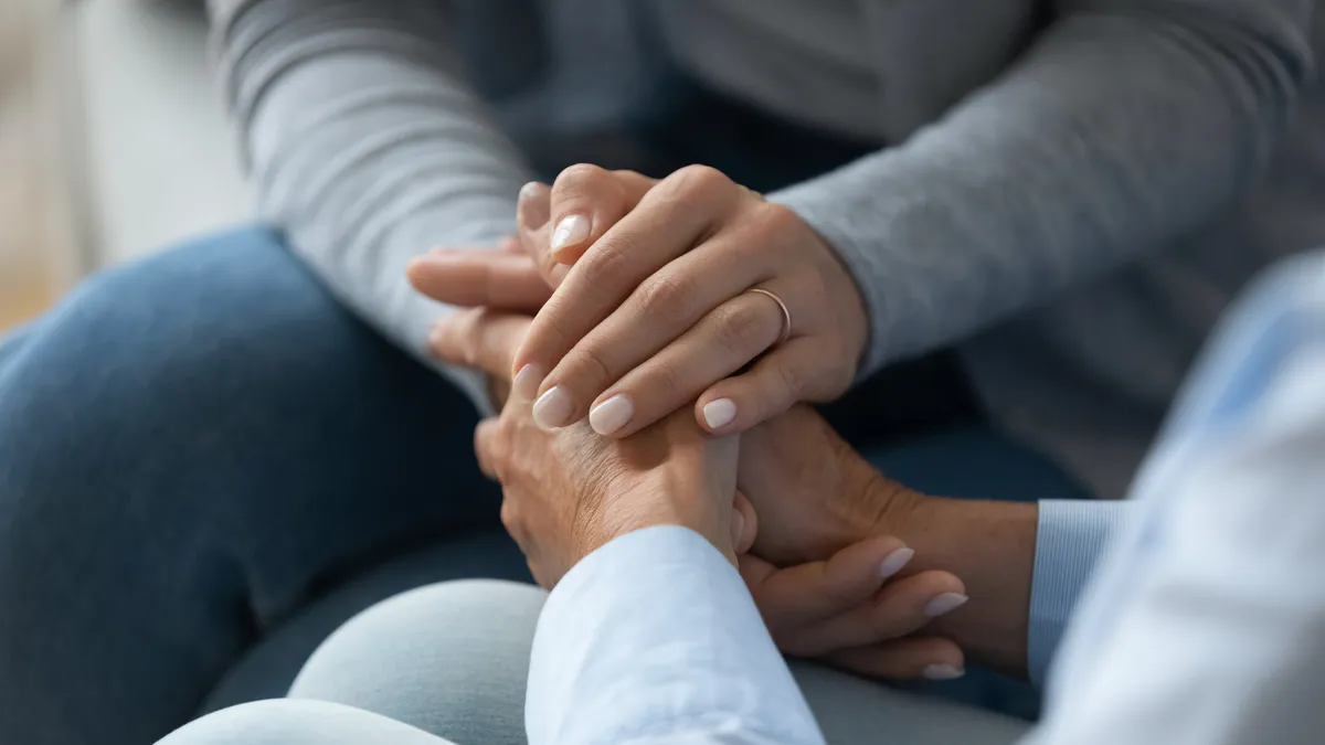 Curano Alltagsbegleitung – Gesundheitsdienst – Erwachsene Tochter streichelt und hält die Hand ihrer alten Mutter (Nahaufnahme).